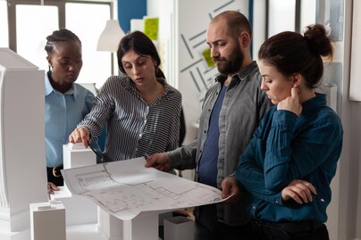 Project management team collaborating in a modern office with blueprints and laptops